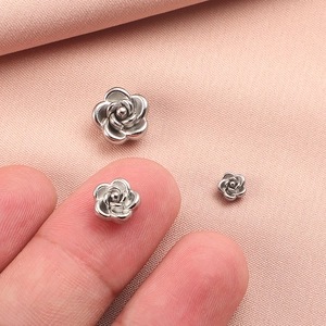 Detailed view of silver stainless steel 3D rose beads in various sizes on pink fabric