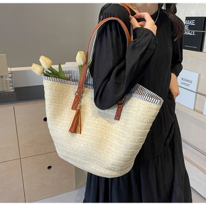Detail of woven straw tote bag featuring brown tassel charm and striped lining with tulips