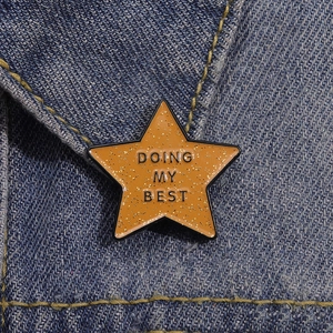 Sparkly orange star enamel pin featuring Doing My Best text on denim fabric