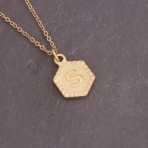 Macro detail of hexagonal gold pendant with letter S engraving on a slim chain