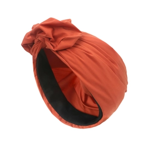 Detail des ziegelroten Knotenturbans mit Stricktextur und schwarzem Innenfutter
