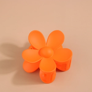 Vue de dessus d'une pince à cheveux mate orange en forme de fleur sur fond beige épuré