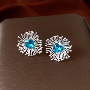 Macro shot of silver stud earrings featuring blue heart crystals and radial sunburst design