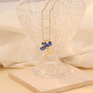 Detail of a gold necklace featuring a blue flower pendant set on a crystal bowl