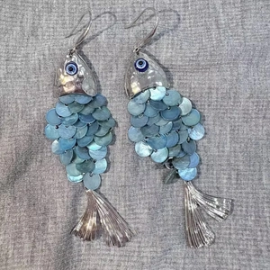 Detailed close-up of fish-shaped earrings featuring blue shell scales and evil eye charm