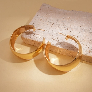 Detailed close-up of gold chunky C-shaped hoop earrings on a textured stone base