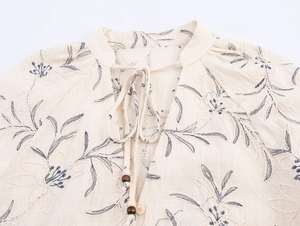 Detailed view of V-neck with blue floral embroidery and wooden beads on linen fabric