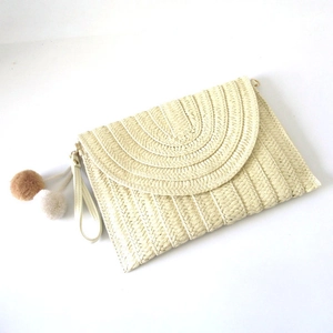 Detail of cream woven clutch featuring layered semicircular texture and plush pom-poms