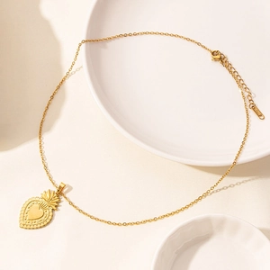 Detail of a 18k gold plated heart pendant necklace with sunburst texture on a ceramic background