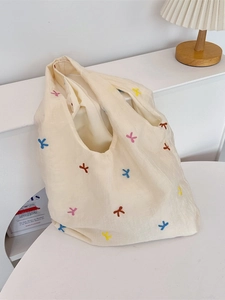Off-white tote bag with colorful embroidered bows and textured light fabric surface