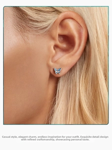 Close-up of small blue butterfly stud earrings in s925 silver worn on model's ear