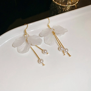 Detail of white petal earrings with small pearl drops and gold stems on a white plate