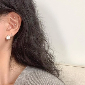 Macro detail of minimalist 925 sterling silver oval stud and chunky hoop earring on ear