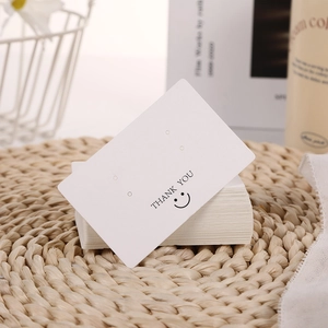 Close-up of white Thank You earrings display cards on a minimalist woven background
