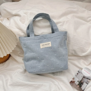 Détail du sac à main en jean bleu clair avec motifs de nœuds tissés et étiquette blanche