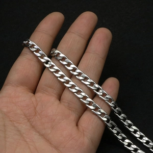 Close-up of high-polish silver cuban link chain held by hand against black background