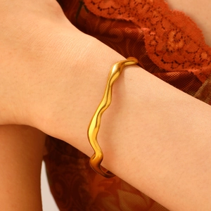 Detail of matte gold wavy bangle on model wrist with minimalist fluid lines