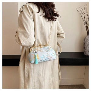 Detailed view of an embroidered floral evening clutch with gold clasp and blue tassel.