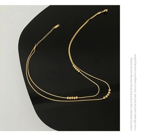 Detail of minimalist 18K gold-plated double-layer snake chain with polished metal beads