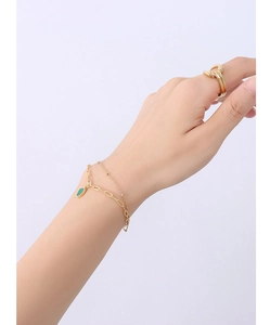 Close-up of gold double-layer bracelet with emerald acrylic pendant on a model's wrist