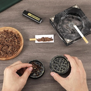 Manual tobacco grinder set with marble ashtray on dark wooden desk scene