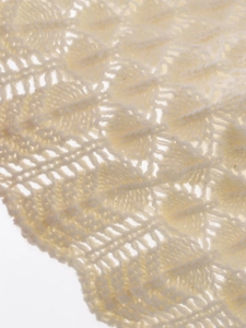 Macro shot of cream white knit fabric featuring delicate hollowed leaf pattern texture