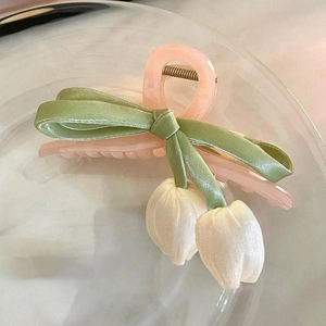 Detail of pink tulip hair claw with satin green bow and silk flower pendants on marble