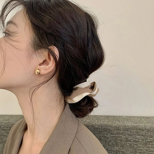 Detailed view of polished gold bean earrings and beige scrunchie worn by a model