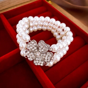 Detail of a triple-layer pearl bracelet featuring a crystal-encrusted clover buckle clasp