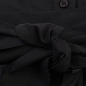 Macro detail of black midi shirt dress showing fabric texture with tied bow and round buttons