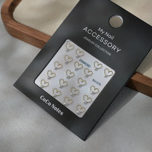 Minimalist gold heart nail stickers with white pearls on a black display card