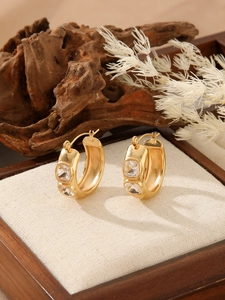 Macro detail of gold-plated earrings with clear zircon stones on a rustic wooden base