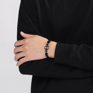 Detail of black woven rope bracelet with anchor pendant on male wrist in studio light