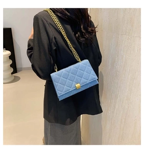 Detail of blue quilted shoulder bag featuring gold chain strap and rectangular clasp