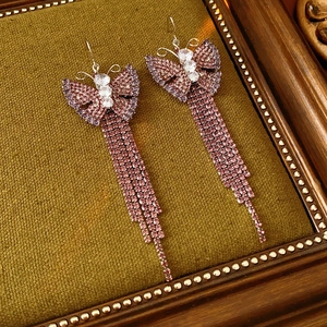 Dettaglio di orecchini a farfalla in zircone rosa con nappe su legno vintage