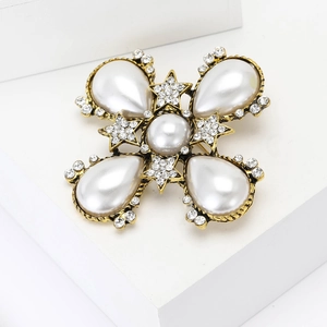 Vintage gold baroque pearl brooch with star-shaped rhinestones on a white geometric stand