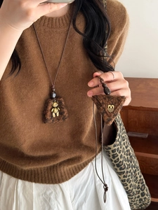 Detailed macro view of the plush brown trapezoid pendant and golden bear on a sweater chain