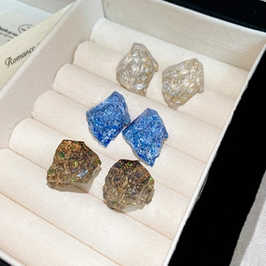 Detailed shot of three pairs of irregular resin stud earrings in a beige velvet jewelry box