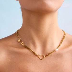 Close-up of gold titanium steel necklace with heart, safety pin and pearl on cuban chain