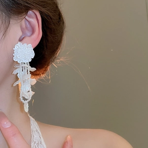 Close-up of elegant white floral tassel earrings with pearls on model in soft light