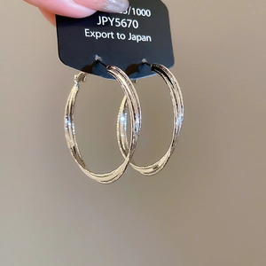 Macro shot of silver triple-layered twisted hoop earrings held with a price tag