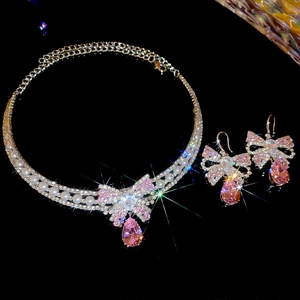 Detailed macro of silver bow jewelry set with pink stones and pearls on black background