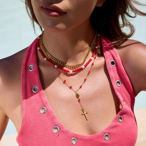 Detail of layered 18K gold stainless steel necklace with red beads and cross charm