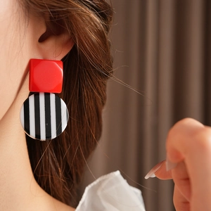 Detail of red square and black-white striped round resin earrings worn by a model