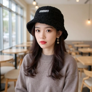 Close-up of black fleece bucket hat with AnoflattoM embroidery in a cozy cafe setting