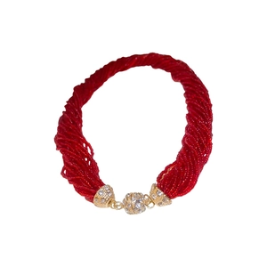 Collana a più strati con perline rosse e chiusura in strass dorati su sfondo bianco