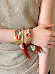 Detail of matte gold open cuff bracelets with silk scarf wrapping on a model's wrist