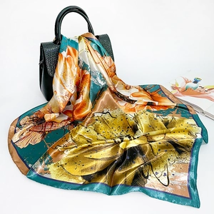 Close-up of silk-like floral square scarf in yellow and orange draped on a black leather bag