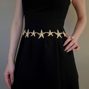 Detail eines goldenen Seestern-Kettengürtels auf schwarzem Kleid für ein luxuriöses Styling