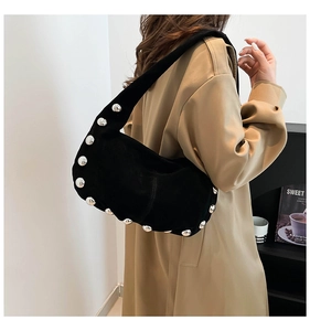 Dettaglio borsa a spalla in camoscio nero con borchie indossata con un cappotto beige